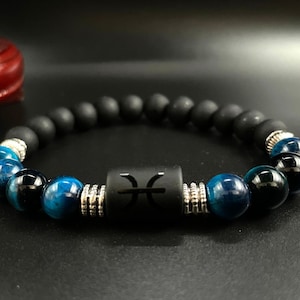 Könnte beinhalten: Ein schwarzes Perlenarmband mit dem Sternzeichen Fische. Das Armband hat schwarze, matte Perlen und blaue Tigeraugenperlen. Silberfarbene Abstandshalter trennen das Sternzeichen und die Tigeraugenperlen.
