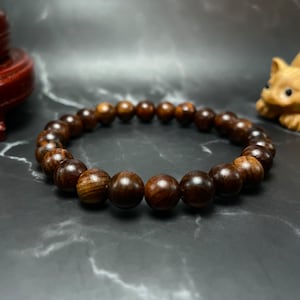 May include: A dark brown wooden beaded bracelet with a circular shape. The bracelet is made of smooth, round beads.