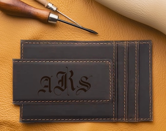 May include: Dark brown leather wallet with a money clip and card slots. The wallet features the engraved initials "ARS" in an elegant font. The stitching is a contrasting light brown. A leather crafting tool is visible in the background.