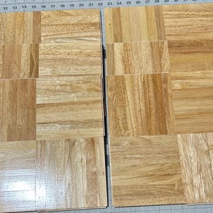 May include: A set of twelve square wooden tiles arranged in two columns of six. Each tile features a natural light brown wood grain pattern with visible horizontal and vertical lines, showcasing a smooth, polished finish and consistent square shape.