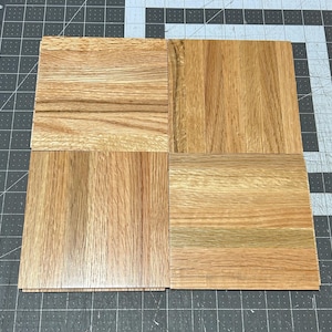 Puede incluir: Cuatro piezas cuadradas de suelo de madera en varios tonos de marr&oacute;n. La veta de la madera es visible en cada pieza.