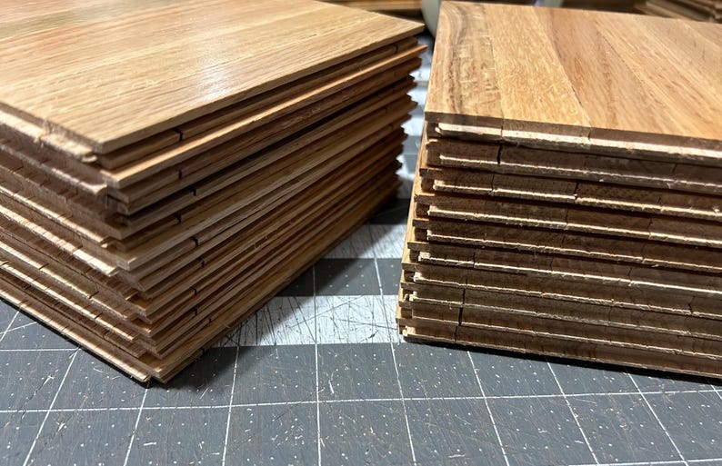 Puede incluir: Dos pilas de tablones de suelo de madera. Los tablones son de color marr&oacute;n claro con un patr&oacute;n de veta de madera. Los tablones est&aacute;n apilados uno encima del otro, creando una forma rectangular.