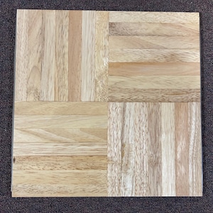 May include: A square wooden cutting board with a light wood grain pattern. The board is divided into four sections, each with a different grain direction, creating a visually interesting design. The wood has a natural, light brown color.