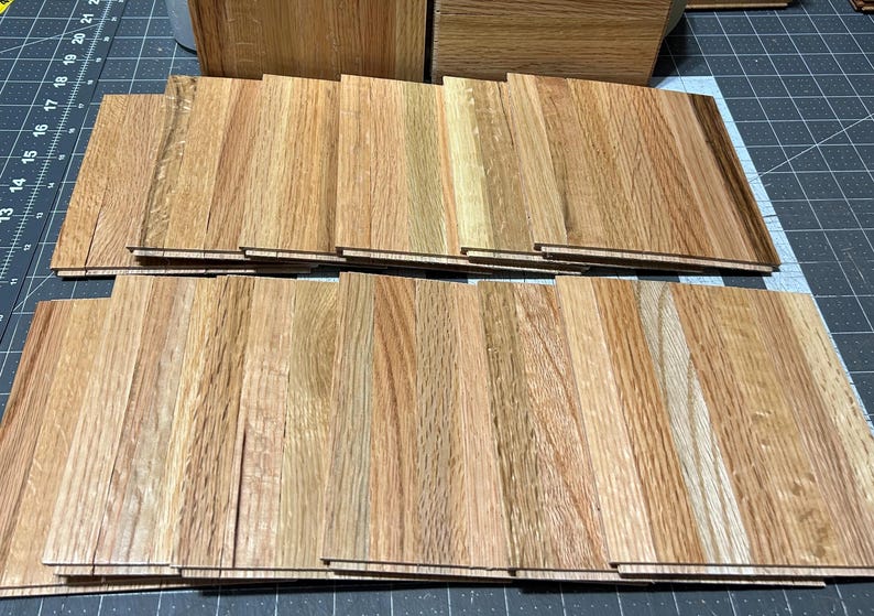 Puede incluir: Una pila de tablones de madera para pisos en varios tonos de marr&oacute;n, con algunos que muestran un patr&oacute;n de veta m&aacute;s claro, casi blanco.