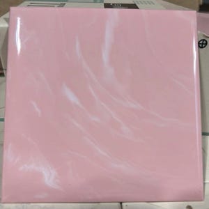 May include: A square, pink tile with a glossy finish. White, swirled patterns are visible across the surface, creating a marbled effect. The tile is likely for home decor or construction.
