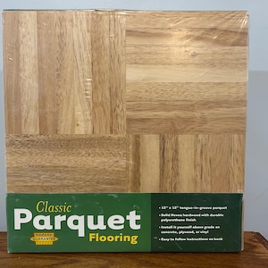 May include: A package of classic parquet flooring. The flooring is made of solid Hevea hardwood with a durable polyurethane finish. The package is wrapped in clear plastic. The flooring is 12 inches by 12 inches.