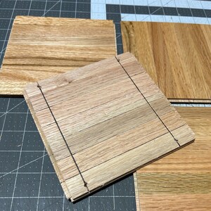 Puede incluir: Cuatro piezas de suelo de madera sin terminar, cada una con un patr&oacute;n de veta de madera natural. Las piezas est&aacute;n apiladas una encima de la otra, con la pieza superior ligeramente desplazada de las dem&aacute;s. La madera es de color marr&oacute;n claro.