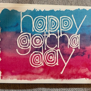 May include: A watercolor card with a gradient of blue, purple, and pink. The card has white text that says "Happy Gotcha Day" in a whimsical font.