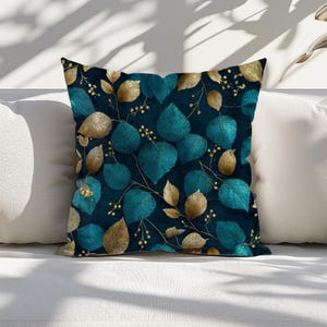 May include: Square throw pillow with a dark teal background and a repeating pattern of teal and gold leaves. The leaves have a textured, embroidered appearance, and the pillow is placed on a white surface.