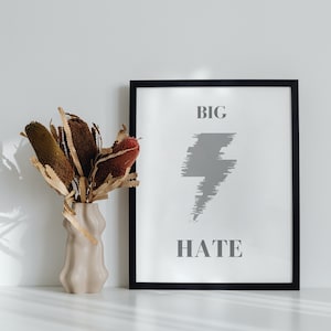Könnte beinhalten: Ein schwarzer gerahmter Druck mit dem Text "BIG HATE" in grauer Schrift und einer stilisierten grauen Blitzdarstellung. Eine Vase mit getrockneten braunen und grünen Blumen steht auf einer weißen Oberfläche vor dem Druck.
