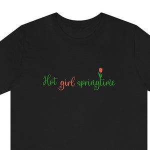 Peut inclure: T-shirt noir avec l'inscription "Hot girl springtime" en vert et rouge, accompagnée d'un petit motif de tulipe rouge et verte. Le t-shirt est à col rond et à manches courtes.
