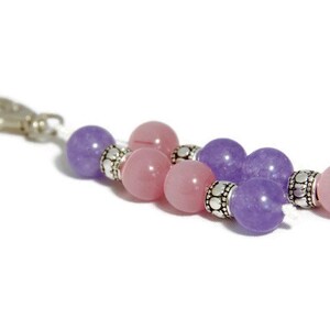 May include: A pink and purple beaded keychain with silver accents. The keychain has a silver clip.