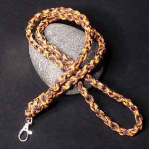 May include: A black, yellow, and orange braided lanyard with a silver clip.