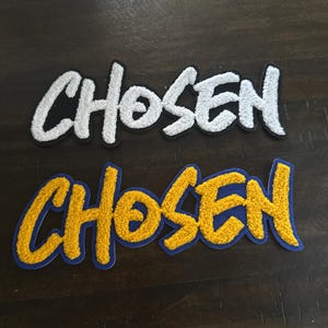 May include: Two embroidered patches featuring the word CHOSEN in a textured, fuzzy script font. The top patch is white with a black border, while the bottom patch is yellow with a blue border. Both patches have a distinct, raised, chenille-like texture.