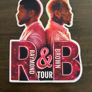 May include: A die-cut patch featuring two men in pink jackets facing away from each other. The text R&B RAYMOND & BROWN TOUR is printed in large white letters over a red and purple galaxy-themed background. The patch has a white stitched border.