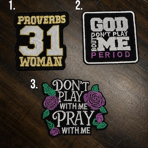 May include: Three embroidered patches on a dark surface. Patch 1 features gold and silver text reading PROVERBS 31 WOMAN. Patch 2 has white and purple text reading GOD DON'T PLAY BOUT ME PERIOD. Patch 3 features white text reading DON'T PLAY WITH ME PRAY WITH ME surrounded by purple roses and green leaves.