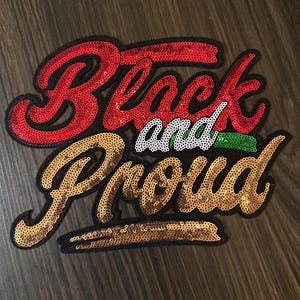 May include: A sequined patch with the words "Black and Proud". The word "Black" is in red sequins, "and" is in white sequins, and "Proud" is in gold sequins. The patch has a black border.