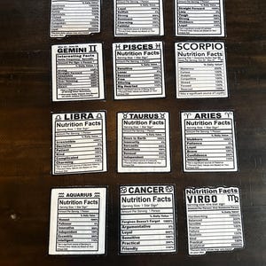 May include: A collection of white rectangular cards with black text, each labeled with a zodiac sign and "Nutrition Facts." The cards list personality traits with percentage values. The signs include Sagittarius, Leo, Capricorn, Gemini, Pisces, Scorpio, Libra, Taurus, Aries, Aquarius, Cancer, and Virgo.