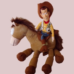 May include: A plush toy of Woody from Toy Story riding a brown horse. Woody is wearing a cowboy hat, yellow shirt, vest, blue jeans, and brown boots. The horse has a brown mane and tail.