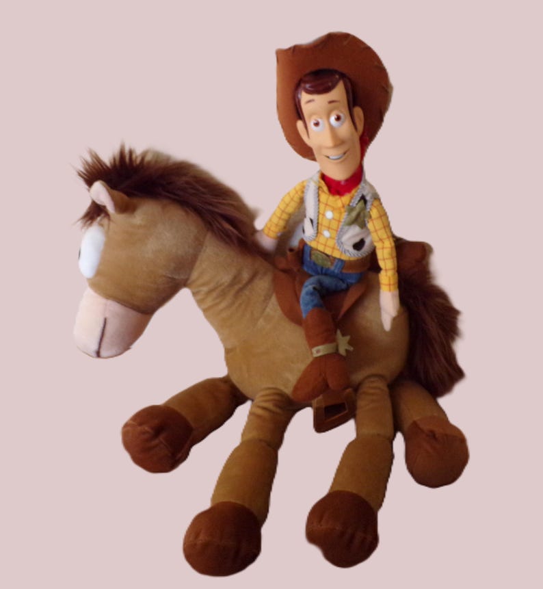May include: A plush toy of Woody from Toy Story riding a brown horse. Woody is wearing a cowboy hat, yellow shirt, vest, blue jeans, and brown boots. The horse has a brown mane and tail.