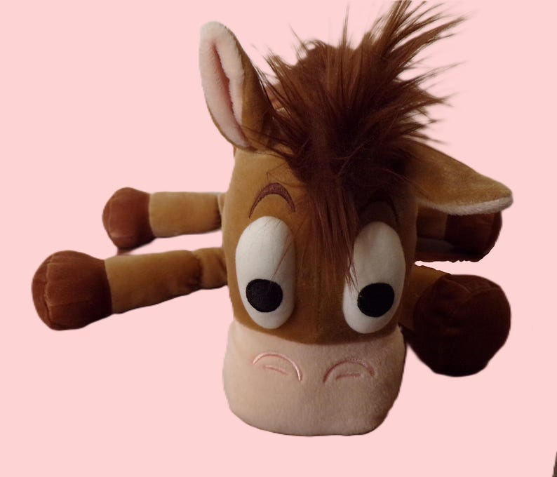 May include: A plush toy depicting a cartoon horse with brown fur, a light pink muzzle, and large, expressive eyes. The toy has a brown mane and four outstretched limbs, creating a playful and inviting appearance.