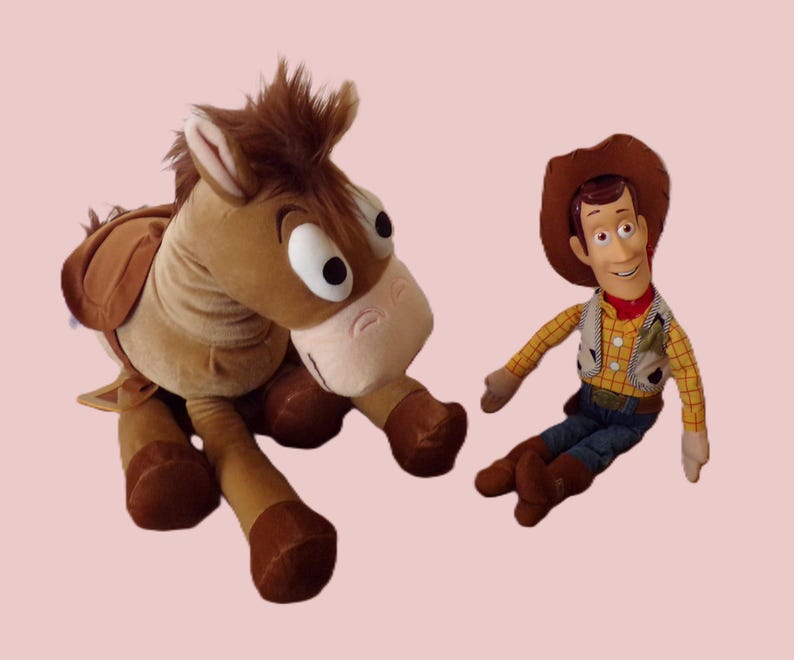 May include: A plush toy set featuring a brown horse and a Woody doll. The horse has a saddle and large eyes. Woody is wearing a cowboy hat, vest, and jeans. The toys are on a light pink background.