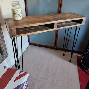 May include: A rustic wooden console table with two shelves and black hairpin legs. The table is made from reclaimed wood and has a natural finish. A candle is sitting on the top shelf.