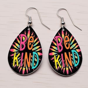 May include: A pair of teardrop-shaped earrings with silver hooks. The earrings are black with a colorful tie-dye design and the words "Be Kind" in a rainbow font.