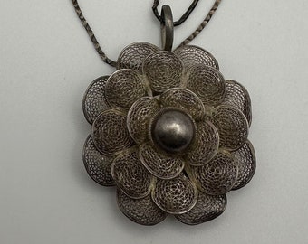 May include: A silver chain necklace with a silver filigree flower pendant. The flower has a round center and is made of delicate wire.