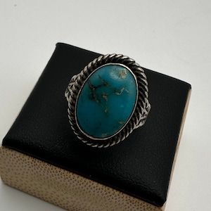 May include: A silver ring with a turquoise stone set in a rope-like design.