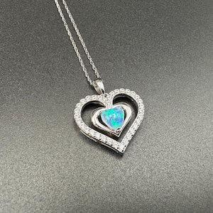 Puede incluir: Collar de plata con un colgante de doble corazón. El corazón exterior está engastado con pequeños cristales transparentes, y el corazón interior presenta una piedra de ópalo azul-verdoso. El colgante cuelga de una delicada cadena de plata, creando un look romántico y elegante.