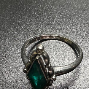 Puede incluir: Un anillo de plata con una piedra preciosa verde engastada en un dise&ntilde;o decorativo. El anillo est&aacute; marcado con "10K 585 1/2" en la banda interior.