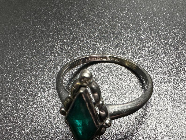 Puede incluir: Un anillo de plata con una piedra preciosa verde engastada en un dise&ntilde;o decorativo. El anillo est&aacute; marcado con "10K 585 1/2" en la banda interior.