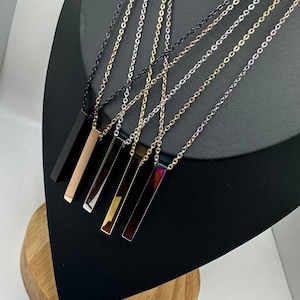 May include: Five silver bar necklaces with different colored bars. The bars are black, rose gold, silver, gold, and iridescent.