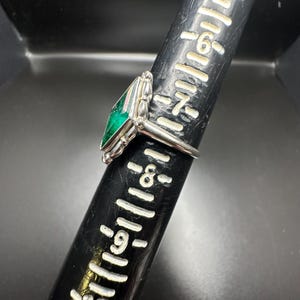 Puede incluir: Un anillo de plata con una piedra preciosa verde engastada en forma cuadrada. El anillo est&aacute; sobre una regla con marcas hasta 25 cm.
