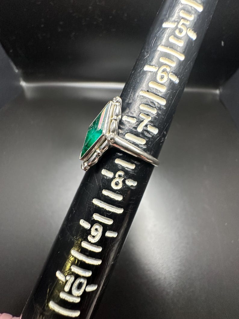 Puede incluir: Un anillo de plata con una piedra preciosa verde engastada en forma cuadrada. El anillo est&aacute; sobre una regla con marcas hasta 25 cm.