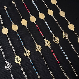 May include: A collection of gold bracelets with different colored beads and charms. Some charms feature the Arabic word for God, while others feature a circular design with Arabic script.