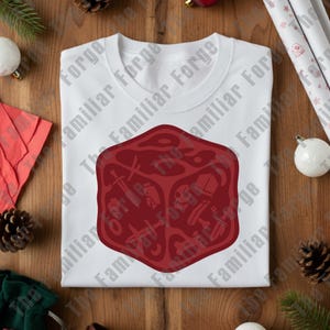 May include: A white t-shirt with a large burgundy die graphic. The die design features symbols like swords and skulls. The shirt is made of a soft material, suitable for casual wear. The text "The Familiar Forge" is printed on the shirt.