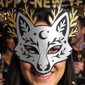 May include: A silver fox mask with black glitter trim and gold antlers. The mask features a crescent moon and star details. Perfect for a masquerade or New Year's Eve celebration.