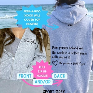 May include: A gray full zip-up hooded sweatshirt with the text "You are enough." on the front and "Dear person behind me, The world is a better place with you in it. -the person in front of you" on the back. The hood is designed to cover the text on the front.