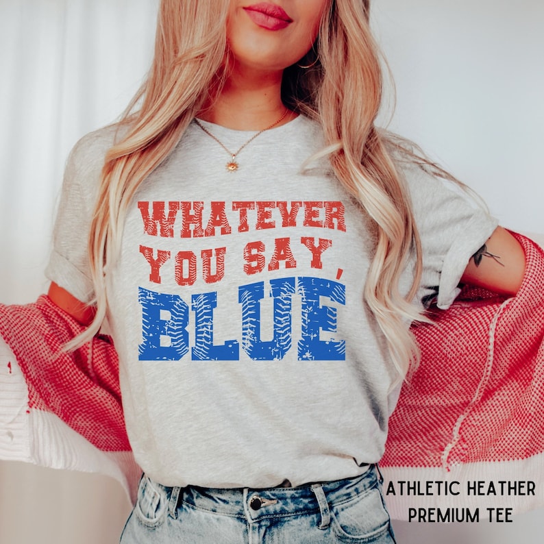 May include: A gray t-shirt with the text "Whatever you say, Blue" in red and blue lettering. The text is distressed and has a baseball-inspired design. The t-shirt is labeled "Athletic Heather Premium Tee".
