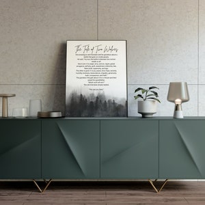 Puede incluir: Una impresión en blanco y negro con una cita sobre dos lobos, uno que representa el bien y el otro el mal. La impresión está enmarcada y colgada en una pared sobre un armario verde con patas doradas. Hay dos lámparas y una planta en maceta sobre el armario.