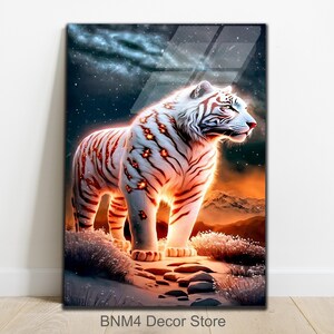 May include: A white tiger with orange stripes stands on a rocky surface. The tiger is illuminated by a bright light, creating a glowing effect. The background is a dark blue sky with stars and a distant mountain range.