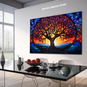 May include: A colorful stained glass style painting of a tree with a sunset in the background. The tree has a thick trunk and many branches with leaves in shades of purple, blue, orange, and yellow. The sunset is a vibrant orange and red with mountains in the distance. The painting is framed and hanging on a white wall in a room with a dining table and chairs.