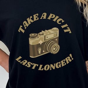 Puede incluir: Camiseta negra con un gráfico de cámara vintage y el texto "Take a pic it last longer!"