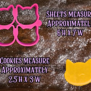 May include: A pink cat-shaped cookie cutter set and a single yellow cookie on a wooden surface dusted with flour. The text indicates the sheet measures approximately 6"H x 7"W, and the cookies measure approximately 2.5"H x 3"W.