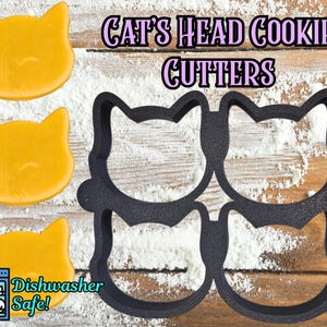 May include: Image of cat-shaped cookie cutters and cookies. The black plastic cutters are in the shape of a cat's head. Three yellow cookies are also visible. Text reads "Cat's Head Cookie Cutters" and "Dishwasher Safe!"