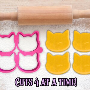 May include: A pink cat-shaped cookie cutter that cuts four cookies at once, with four yellow cat-shaped cookies and a wooden rolling pin. The text "CUTS 4 AT A TIME!" is at the bottom.