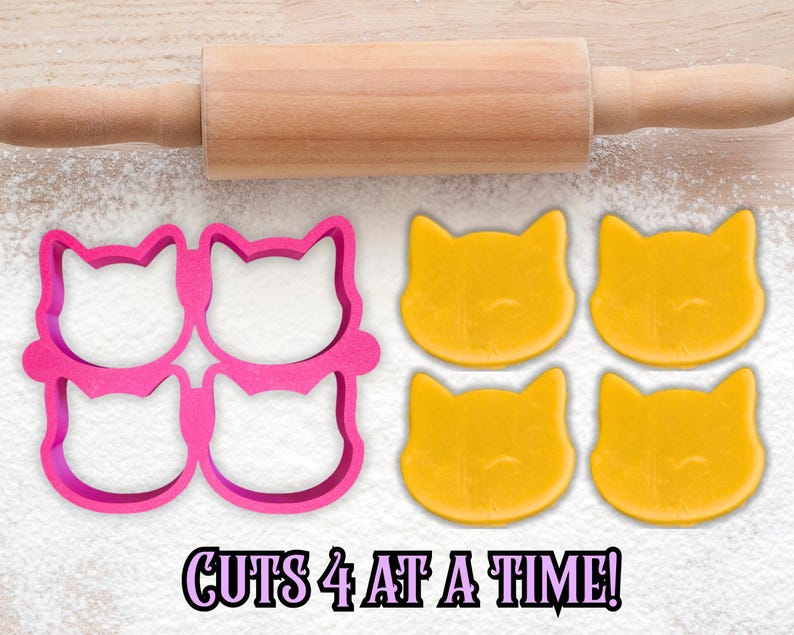May include: A pink cat-shaped cookie cutter that cuts four cookies at once, with four yellow cat-shaped cookies and a wooden rolling pin. The text "CUTS 4 AT A TIME!" is at the bottom.