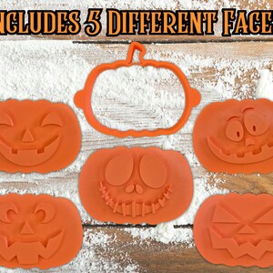 Puede incluir: Cortadores de galletas con forma de calabaza naranja con cinco caras talladas diferentes, junto con un contorno de calabaza. El texto "INCLUDES 5 DIFFERENT FACES!" est&aacute; en la parte superior. Los cortadores est&aacute;n sobre una superficie de madera con polvo blanco.